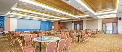 A conference room with round tables and chairs, a projector screen, and a carpeted floor.