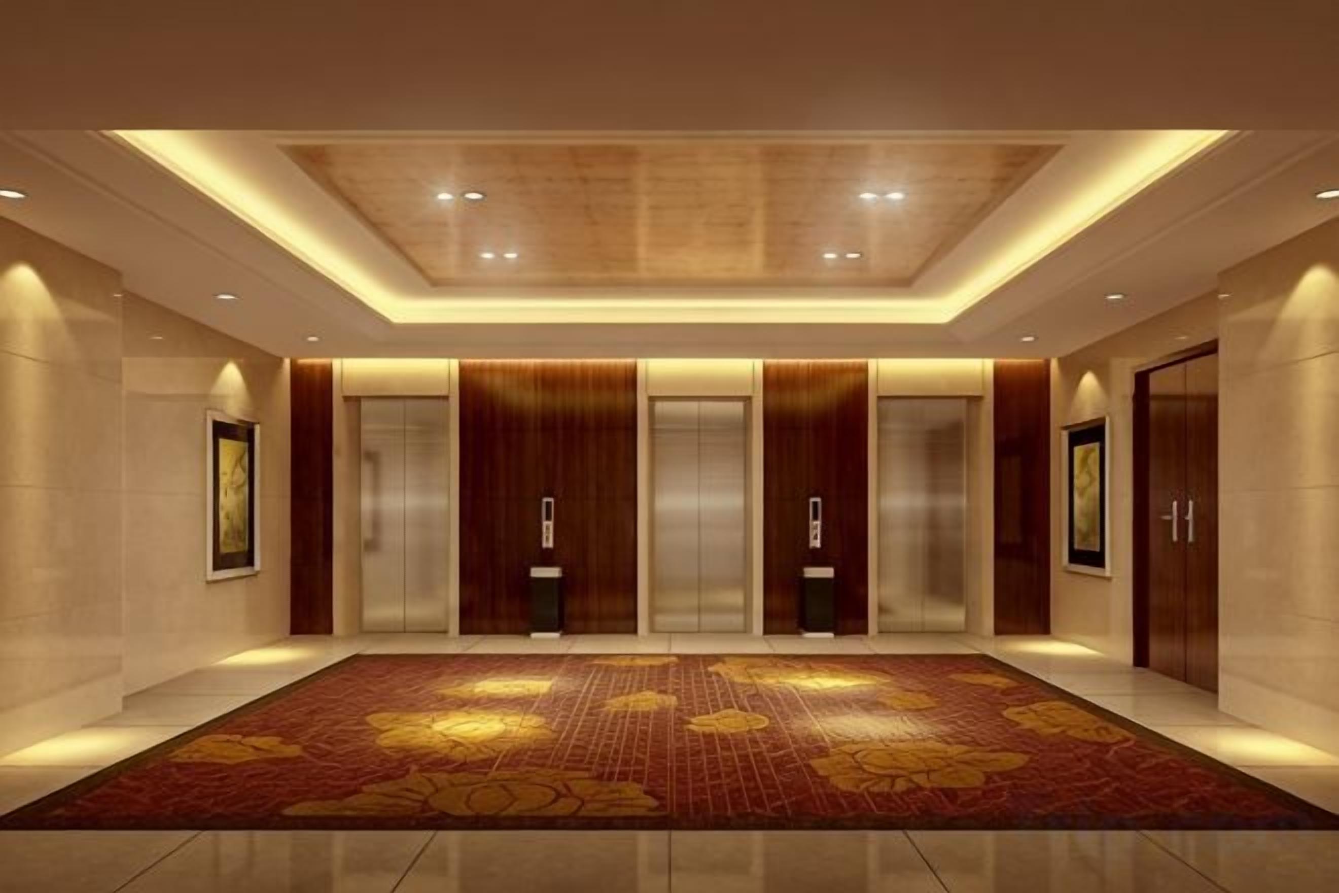 A hotel lobby with a large carpet, elevators, and framed artwork on the walls.
