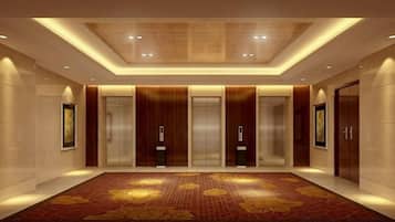 A hotel lobby with a large carpet, elevators, and framed artwork on the walls.