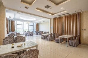 Une salle de conférence d’hôtel avec plusieurs tables et chaises, de grandes fenêtres et un lustre.