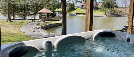 A hot tub with a view of a lake, a gazebo, and a grassy area with trees.