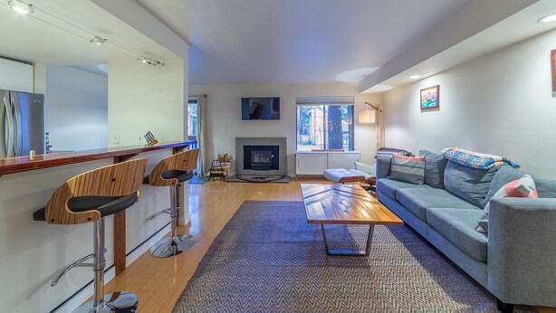A modern living room with a fireplace, a sofa, a coffee table, and a bar area with stools. - Ultra Modern Mammoth Mtn 1 Bdrm WIFI, Spa, 2 cars (Mammoth Lakes)