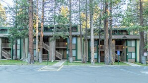 A multi-story building with a green and beige exterior, surrounded by tall trees. - Ultra Modern Mammoth Mtn 1 Bdrm WIFI, Spa, 2 cars (Mammoth Lakes)