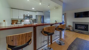A modern kitchen with white cabinets, stainless steel appliances, and a wooden bar area with bar stools. - Ultra Modern Mammoth Mtn 1 Bdrm WIFI, Spa, 2 cars (Mammoth Lakes)