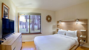 A bedroom with a bed, a TV, a window with a view of trees, and a sunburst wall decoration. - Ultra Modern Mammoth Mtn 1 Bdrm WIFI, Spa, 2 cars (Mammoth Lakes)