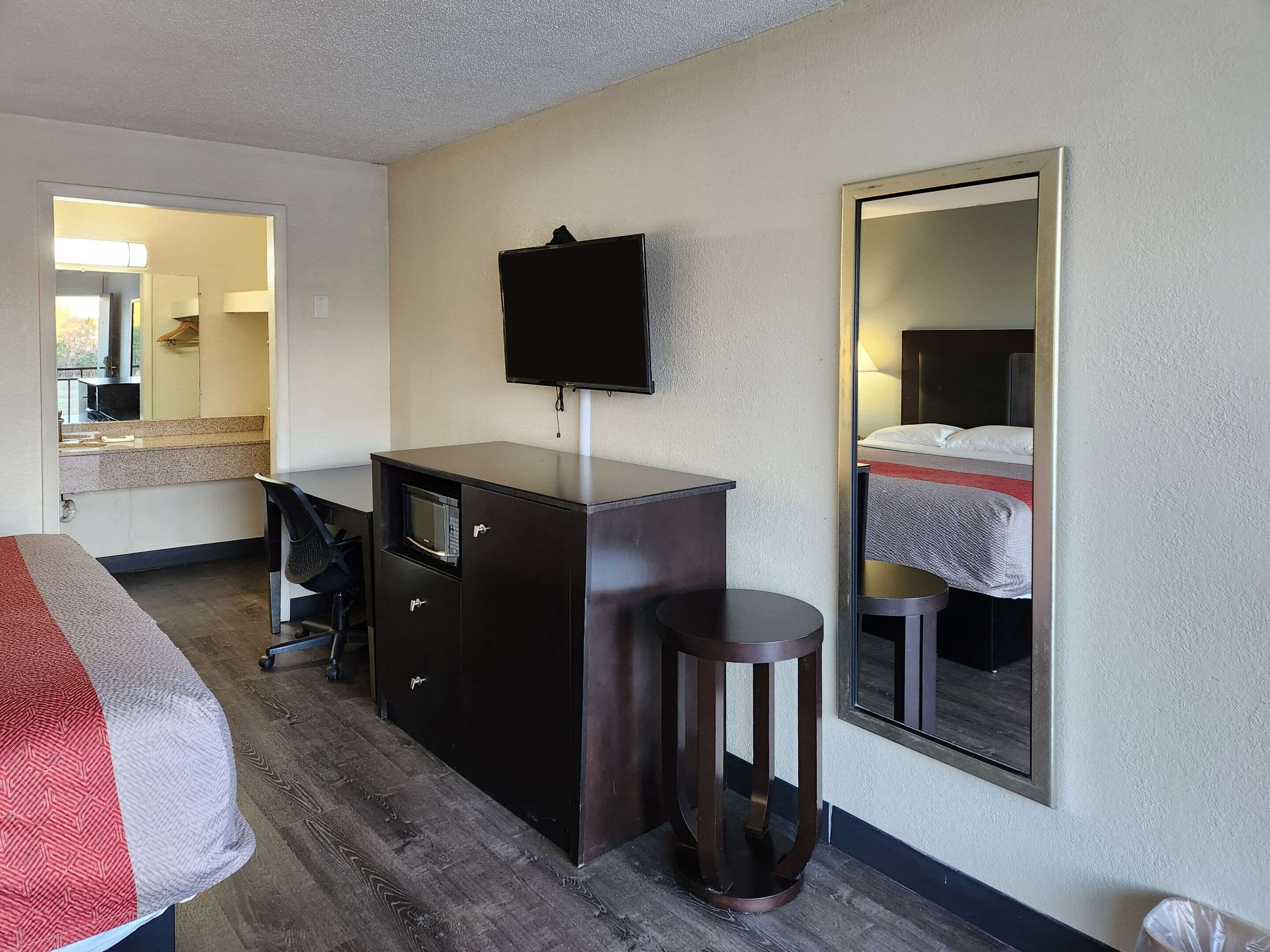 Una habitación de hotel con una cama, un escritorio con una silla, un aparador, un espejo y un televisor.
