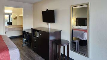 Una habitación de hotel con una cama, un escritorio con una silla, un aparador, un espejo y un televisor.