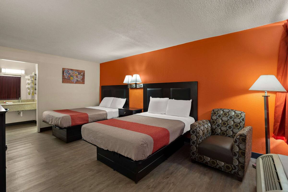 A hotel room with two beds, a chair, a desk, and a mirror.