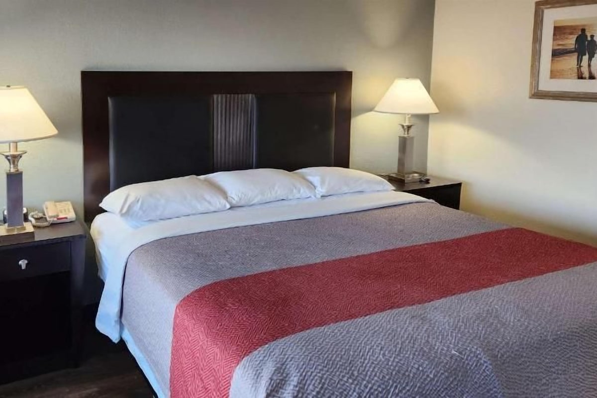 A hotel room with a bed, two bedside tables, lamps, and a painting on the wall.