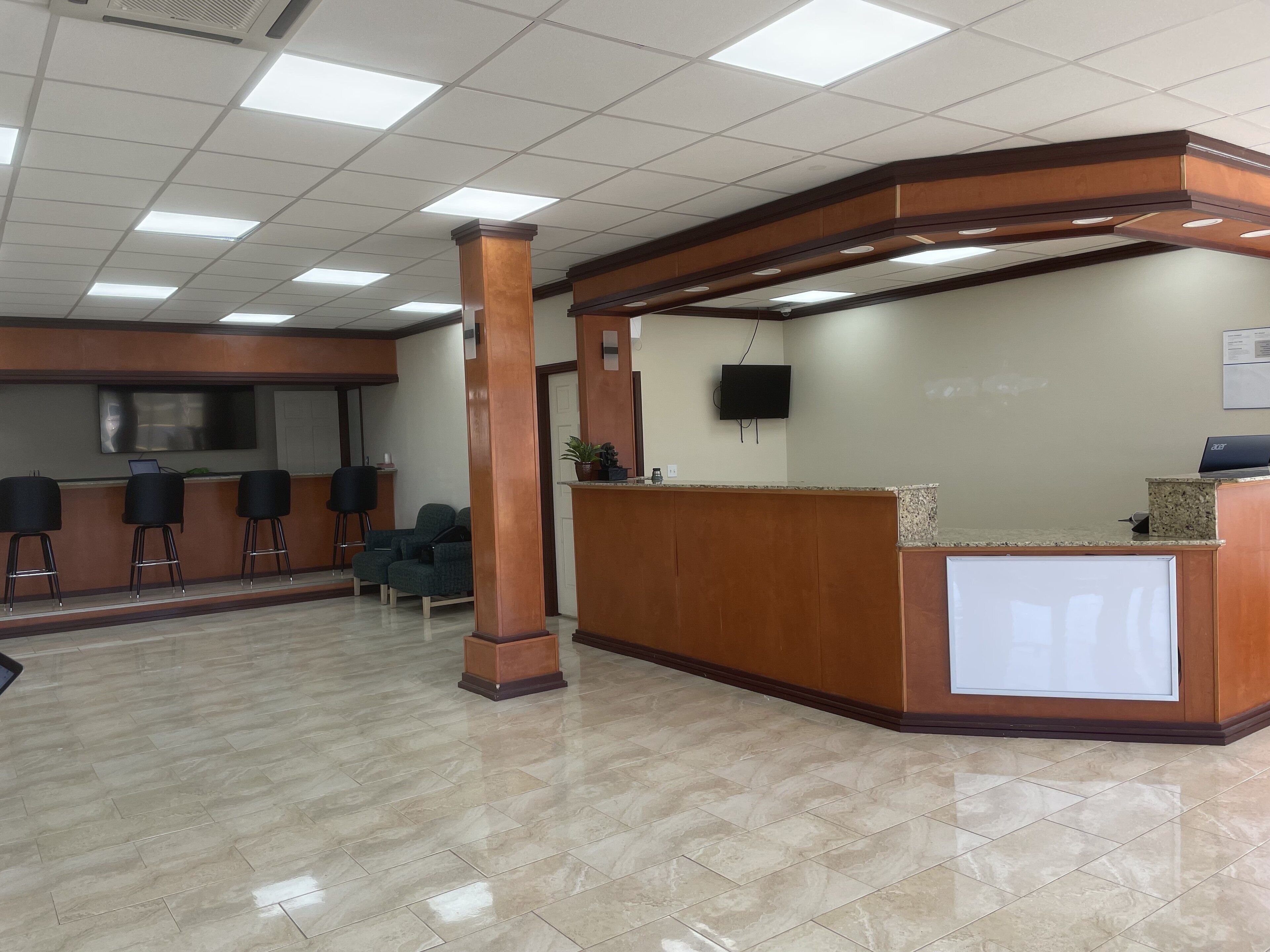 A reception area with a curved wooden desk, a flat-screen TV, and a seating area with chairs.
