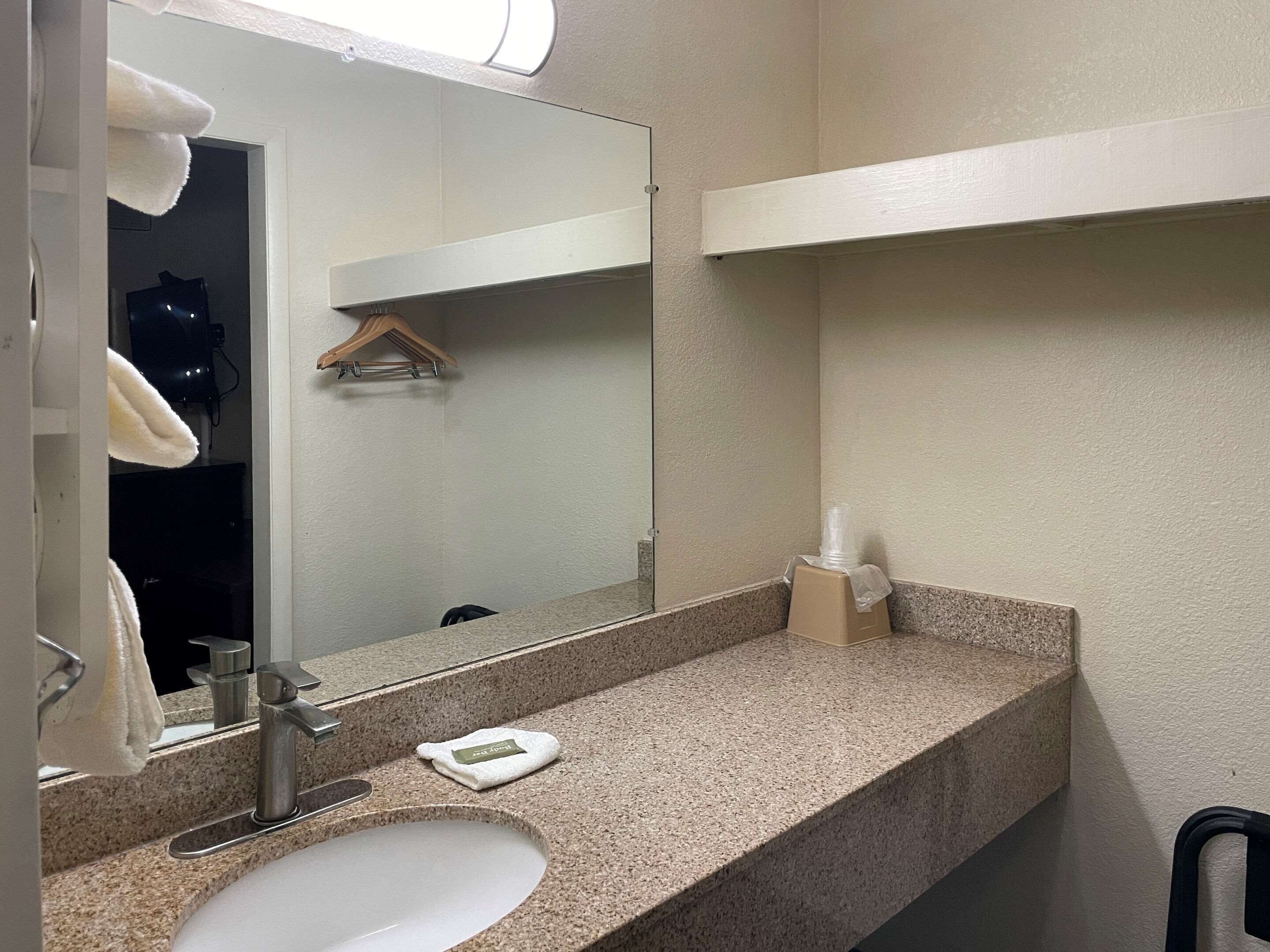 A bathroom with a granite countertop, a sink, a mirror, a towel rack, and a soap dispenser.