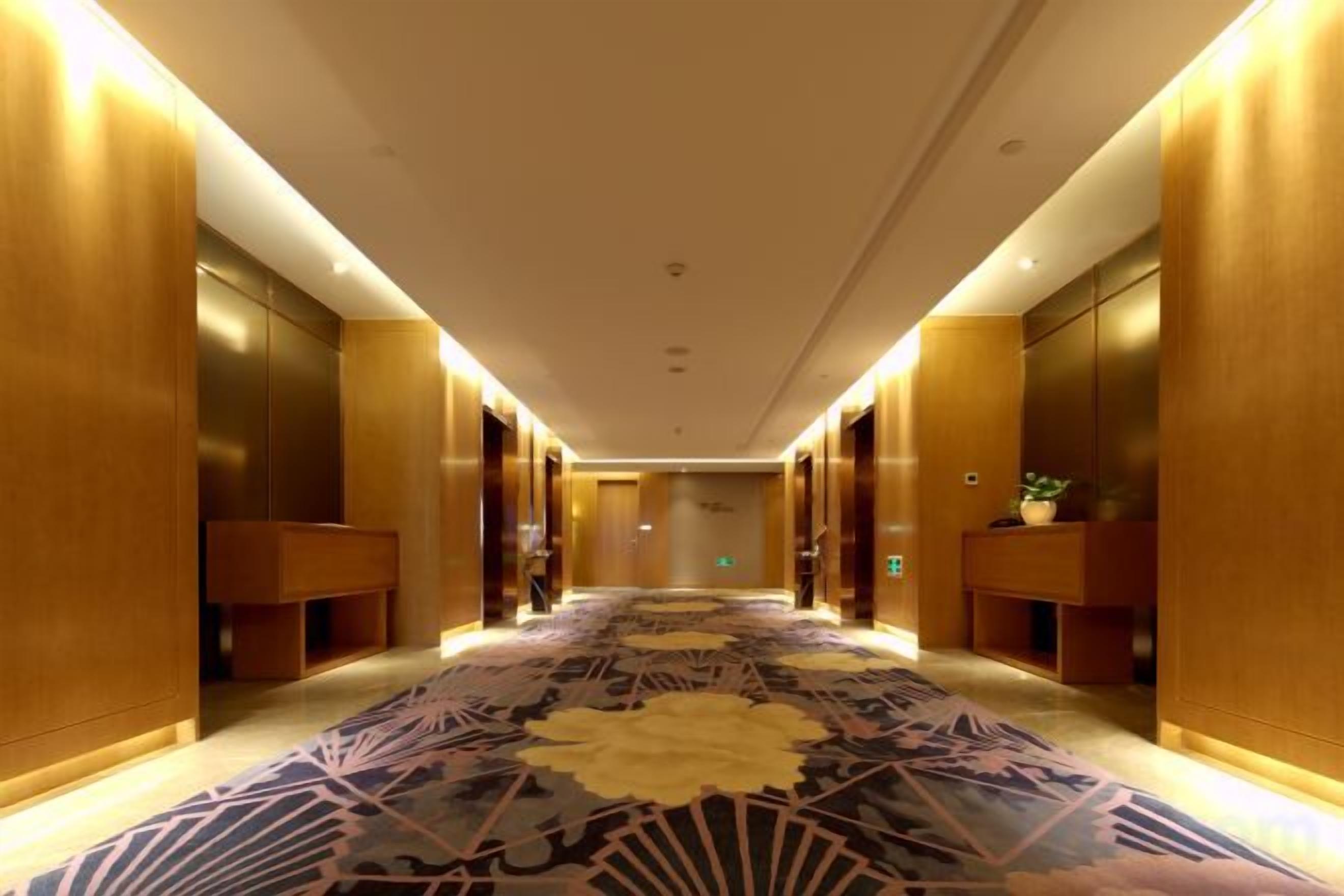 A hotel corridor with wooden walls, a patterned carpet, and a bench.