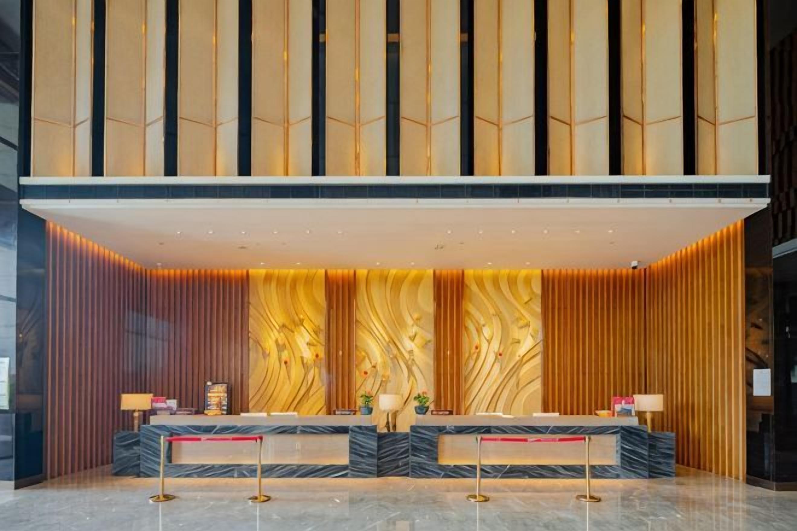 A reception area with a marble counter, two receptionists, and a modern design with vertical wooden panels.