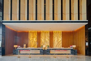 A reception area with a marble counter, two receptionists, and a modern design with vertical wooden panels. - Ruixiang Hotel (Fushun)