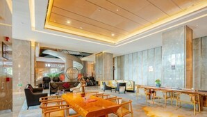 A spacious hotel lobby with a long wooden table, comfortable seating, and a modern ceiling design. - Ruixiang Hotel (Fushun)