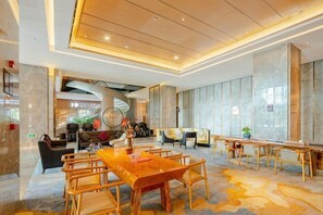 Un hall d’hôtel spacieux, avec une longue table en bois, des sièges confortables et un design moderne au niveau du plafond.