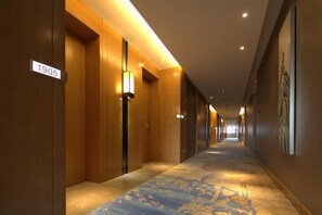 Un pasillo de hotel con puertas de madera, placas de números de habitación y una alfombra estampada.