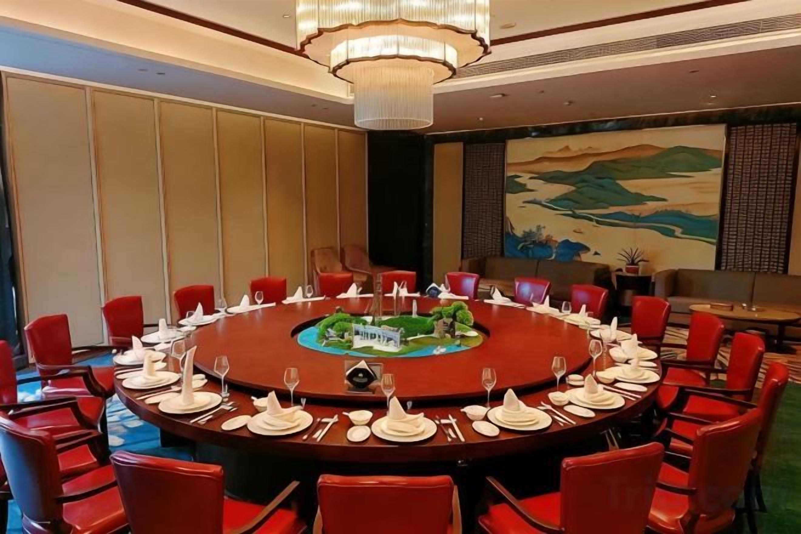 A conference room with a round table, red chairs, and a chandelier.