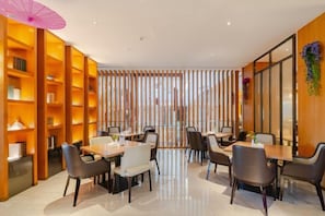 A modern dining area with tables and chairs, a wooden bookshelf, and a decorative partition. - Ruixiang Hotel (Fushun)