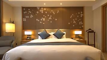 Habitación de hotel con una cama grande, dos lámparas de noche, una silla y un panel decorativo en la pared.