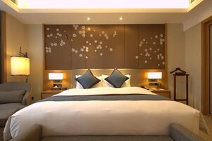 Habitación de hotel con una cama grande, dos lámparas de noche, una silla y un panel decorativo en la pared.