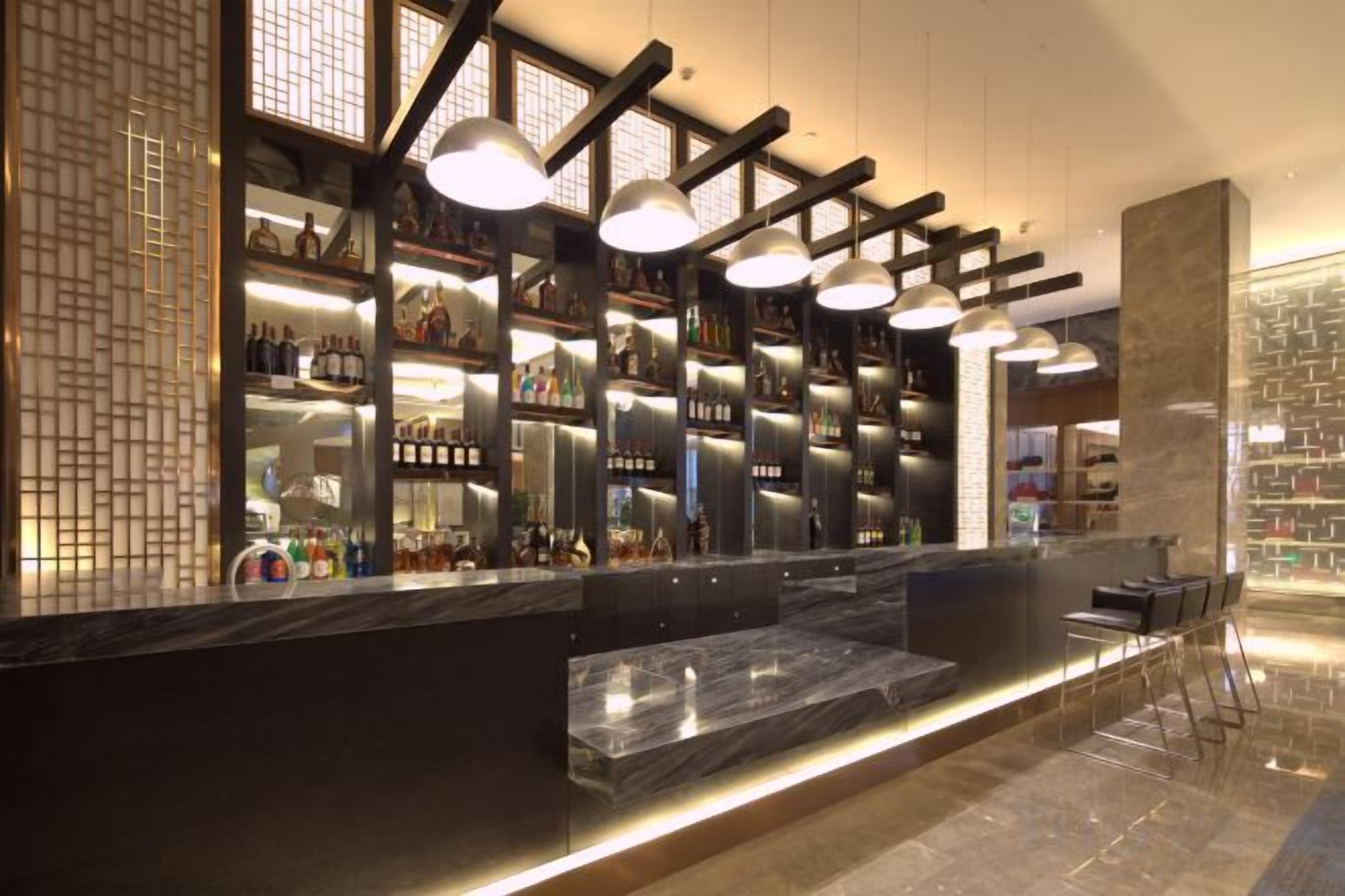 A bar area with shelves of bottles, a marble counter, and hanging pendant lights.