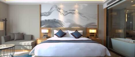 A modern hotel room with a large bed, a sofa, a small round table, and a large window.