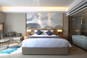 Una habitación de hotel moderna con una cama grande, un sofá, una mesita redonda y un ventanal amplio.