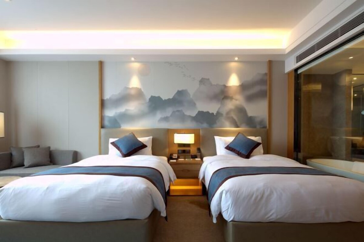 A hotel room with two beds, a large window, and a wall-mounted artwork.