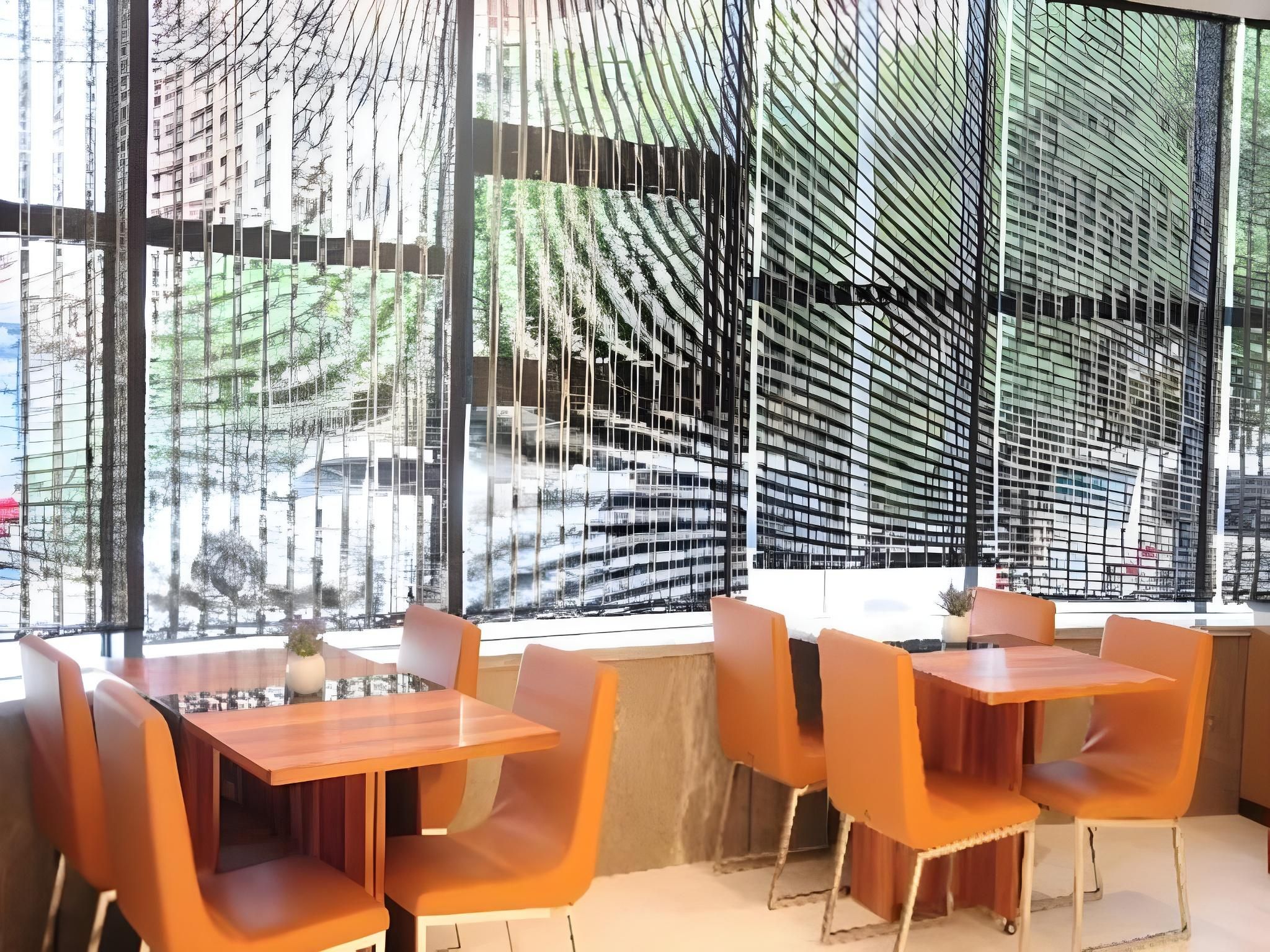 Comedor con mesas y sillas, ventanas amplias con vistas a edificios y árboles, y un diseño arquitectónico moderno.