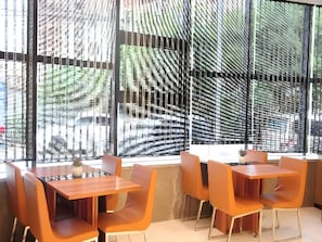 A dining area with tables and chairs, large windows with a view of buildings and trees, and a modern architectural design. - Lavande Hotel (Zhuzhou)