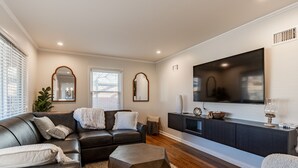 A modern living room with a dark leather sofa, a geometric coffee table, and a flat-screen TV on a dark cabinet.