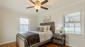 A bedroom with a wooden bed, a ceiling fan, a bedside table with a lamp, and a window with blinds.