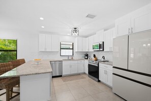 A modern kitchen with white cabinetry, a central island, stainless steel appliances, and a view of greenery outside.