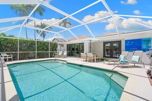 A pool area with a clear blue pool, sun loungers, and a covered seating area.
