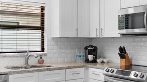 A kitchen with white cabinets, a stainless steel sink, a coffee maker, and a microwave.