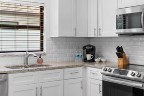 A kitchen with white cabinets, a stainless steel sink, a coffee maker, and a microwave.