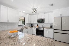 Cozinha moderna com armários brancos, bancada de granito, forno embutido, micro-ondas e geladeira.