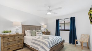 A bedroom with a bed, nightstands, a ceiling fan, a window with curtains, and a chair.