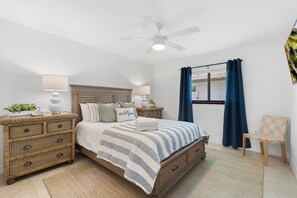 A bedroom with a bed, nightstands, a ceiling fan, a window with curtains, and a chair.