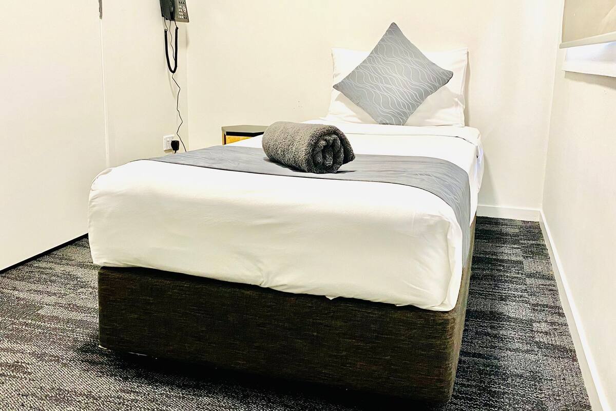 Cama bem arrumada com almofada cinza e toalha cinza enrolada por cima.
