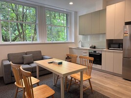 A modern kitchen with a dining area, large windows, and a view of trees.