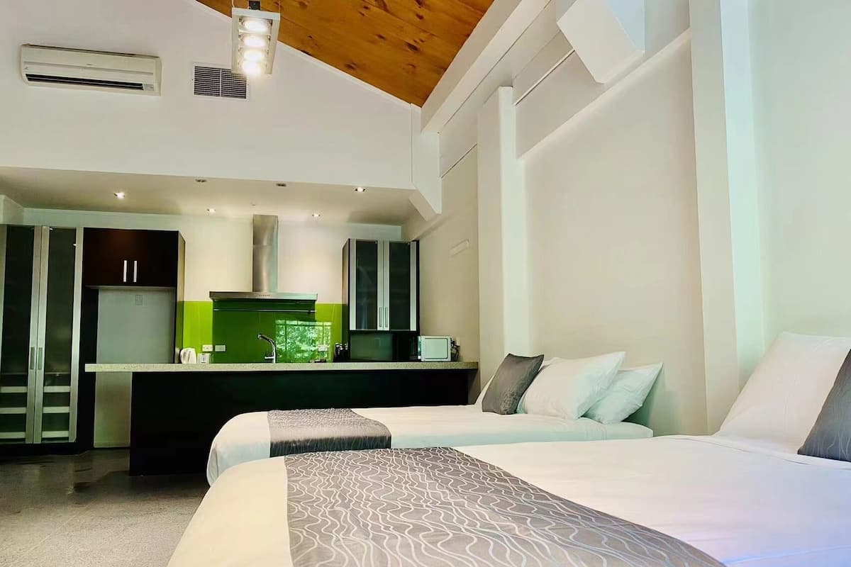 Quarto de hotel moderno com uma cama grande, uma kitchenette e teto de madeira.
