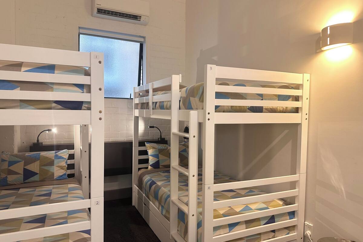 Quarto com beliches, janela, ar condicionado e luminária fixada na parede.