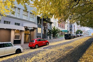 A street with parked cars, a red car with 'cityhop' branding, and a building with a 'GAMMA HOTEL' sign.