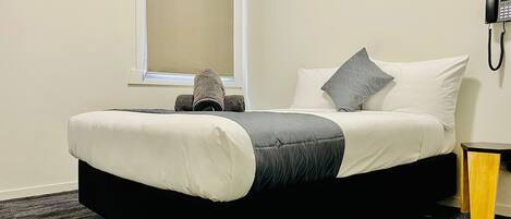 A hotel room with a bed, a window, a telephone, and a small wooden side table.