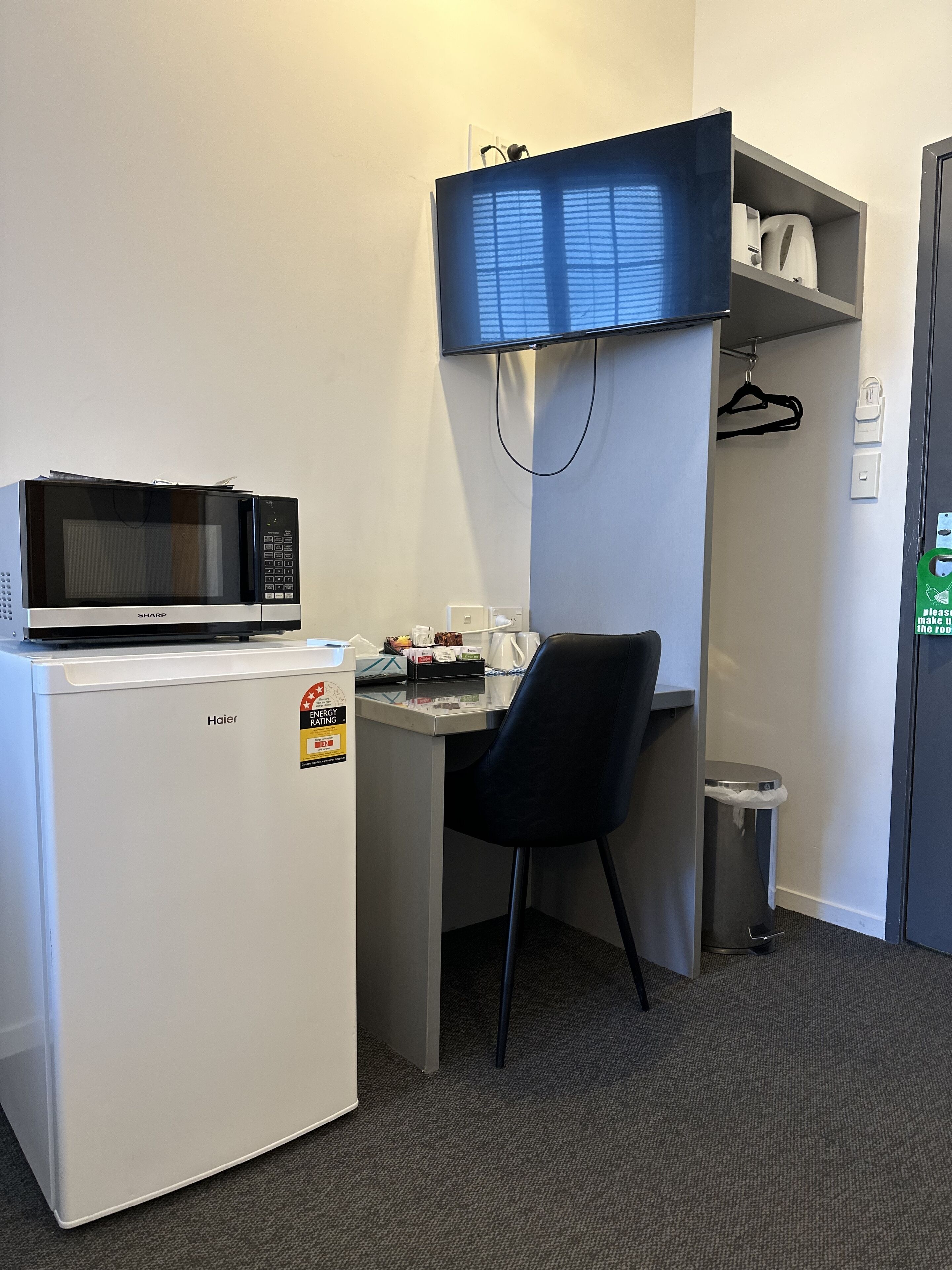Uma cozinha compacta equipada com micro-ondas, um pequeno frigorífico, uma cadeira, uma secretária e uma televisão fixada sobre a secretária.