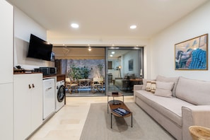 A modern living room with a sofa, a coffee table, a TV, and a washing machine in the background.