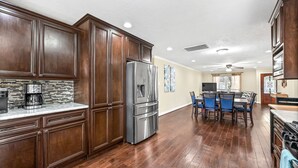 A spacious kitchen with dark wooden cabinets, a stainless steel refrigerator, and a tiled backsplash.