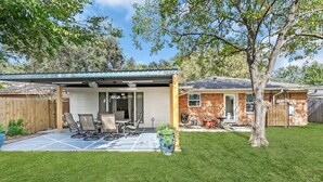 A backyard with a covered patio, a wooden deck, and a brick house.